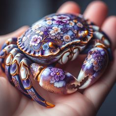 a hand holding a purple and white crab in it's right hand with flowers painted on its body