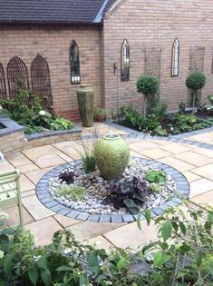 an outdoor garden with rocks and plants in the center, surrounded by brick walls and green chairs