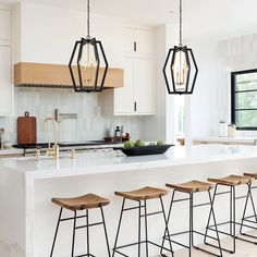 a kitchen island with four stools in front of it and three lights hanging from the ceiling