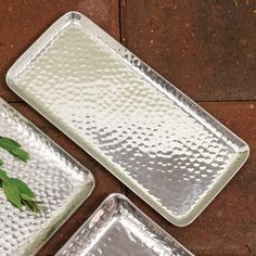 three metal trays sitting on top of a brown tile floor next to a plant