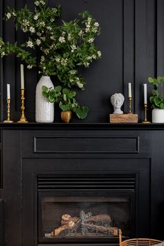 a fireplace with flowers and candles on it in a black living room, next to a wicker basket