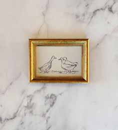 two birds kissing each other in a gold frame on a marble surface with white and black veining