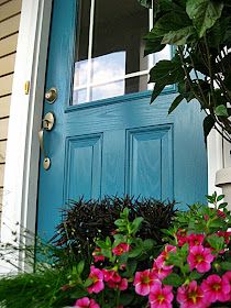 a blue front door with pink flowers in the planter next to it and a window