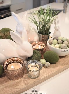 a wooden tray topped with candles and bunny figurines next to bowls filled with eggs