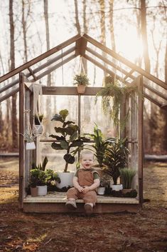 a baby sitting in front of a greenhouse with potted plants on the outside and inside