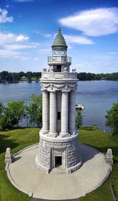 a clock tower sitting on top of a lush green field next to a lake with boats in the water