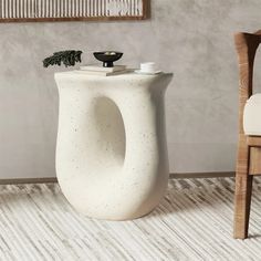 a white vase sitting on top of a wooden floor next to a chair and table