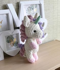 a crocheted stuffed unicorn sitting on top of a table next to two frames