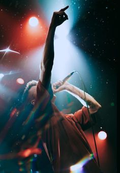 a man standing on stage with his arms in the air and holding a microphone up