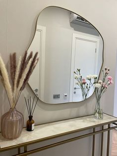 a mirror sitting on top of a table next to vases with flowers in it