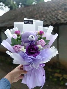 a person holding a purple teddy bear with flowers in it's hand and a tag on the back