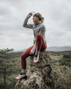 a woman sitting on top of a rock with her legs crossed and wearing red leggings