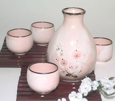 a pink vase sitting on top of a wooden table next to cups and saucers