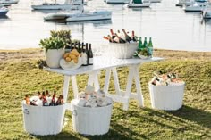 several buckets filled with bottles and snacks on a table in the grass near water