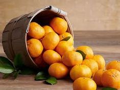 a bucket filled with lots of oranges on top of a wooden table next to leaves