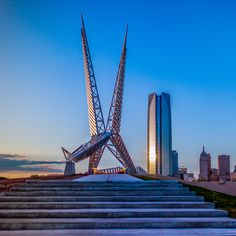 the stairs lead up to an artistic sculpture in front of a cityscape at sunset