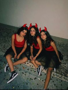 three women in devil costumes sitting on the ground