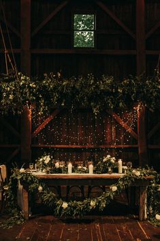 the table is set up with candles and greenery for an elegant wedding reception in a barn