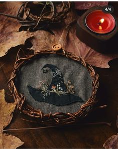 an embroidered witch's hat on top of leaves next to a candle