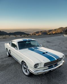 an old white mustang with blue stripes parked in the desert