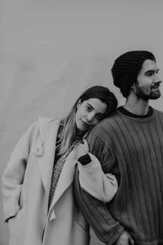 a man and woman standing next to each other in front of a white wall wearing hats