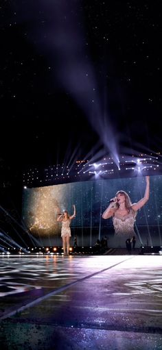 two women are performing on stage with their arms in the air and lights shining above them