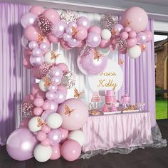 a table topped with balloons and cake next to a wall covered in pink and white