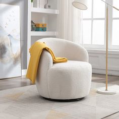 a white chair with a yellow blanket on it in front of a window and a lamp