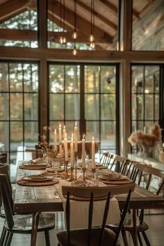 a dining room table is set with place settings and lit candles in front of the windows