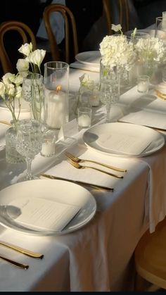 the table is set with white flowers and place settings