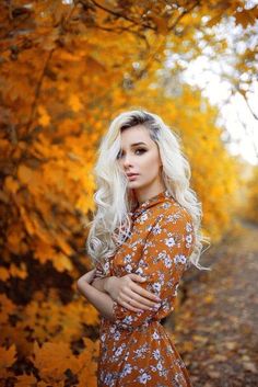 a woman standing in front of trees with yellow leaves on it's sides and her arms crossed