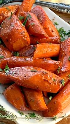 a white plate topped with sliced carrots and parsley on top of a wooden table