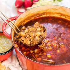 a ladle full of chili and beans being spooned into a pot filled with soup