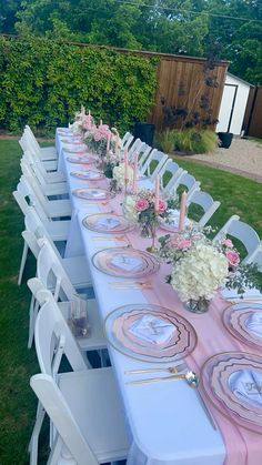 a long table is set with pink and white flowers, plates and napkins on it