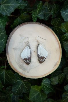 a pair of earrings sitting on top of a leaf covered table next to green leaves