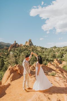 a bride and groom dancing on top of a mountain in front of the desert landscape