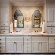 two sinks and mirrors in a bathroom with white cabinetry, marble counter tops and gray tile flooring