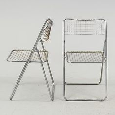 two metal chairs sitting next to each other on a white surface with one chair facing the camera