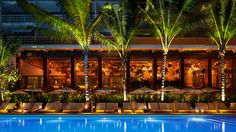 an outdoor pool with lounge chairs and umbrellas next to the swimming pool at night