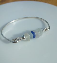 Sea Glass Bangle - Sterling Silver, Seaham Sea Glass, Blue Accent Sea Glass Effect Frosted Bead.  The width of the D shape silver section of the bangle is 2mm.  The size of the bangle width is 7cm approx and would suit a medium to large wrist. Please measure the widest part of your hand or your own bangles to check for size.  The bangle is handmade from sterling silver ( solid 925 silver ). All my silver is sourced from a reputable UK supplier and is made from recycled silver. The beaded section Nickel-free Silver Glass Bracelet, Silver Glass Bracelets With Round Beads, Nickel Free Sterling Silver Beaded Bangle, Adjustable Blue Sterling Silver Bangle Bracelet, Handmade Blue Sterling Silver Bangle Bracelet, Blue Sterling Silver Bangle Bracelet, Seaglass Jewellery, Blue Enamel Earrings, Sea Glass Beads