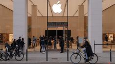 people are walking and riding bikes in front of an apple store with the doors open