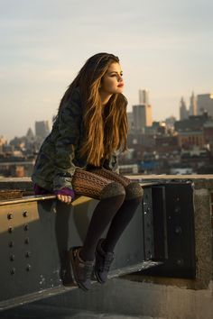 a woman sitting on top of a building next to a luggage bag in front of her