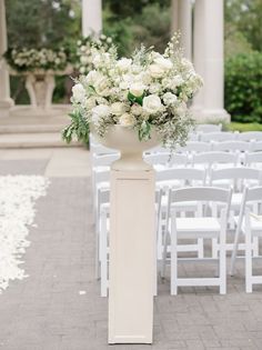 an outdoor ceremony with white chairs and flowers in vases on the side walk way