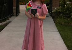 a woman in a pink dress is holding a book and standing on the side walk