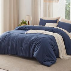 a bed with blue comforter and pillows in a room next to a window on the floor