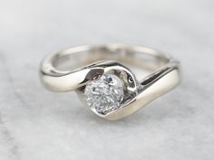 a white gold engagement ring with a diamond in the center on a marble table top