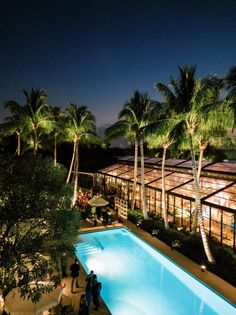 an outdoor swimming pool surrounded by palm trees and people standing around it at night time