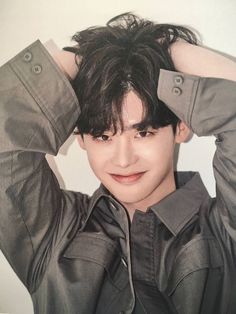 a young man with black hair and grey shirt holding his hands to his head while posing for the camera