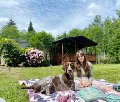 a woman and her dog sitting on a blanket in front of a house with pink flowers