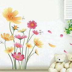 a teddy bear sitting next to a wall with flowers on it